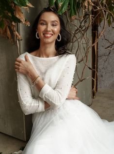 a woman in a white dress is posing for the camera with her arms crossed and smiling