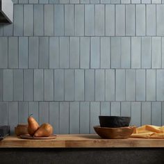 a wooden table topped with bowls filled with fruit next to a wall covered in grey tiles