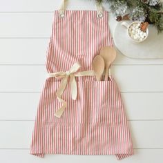 a pink and white striped apron with wooden spoons on it next to a potted plant