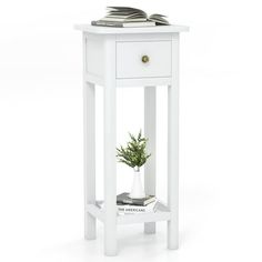 a white end table with a book on top and a potted plant in the corner