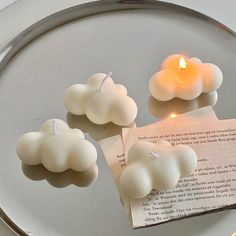 three candles on a plate with a piece of paper next to it that has been placed in the shape of clouds