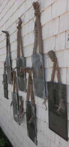 several pieces of art hanging on the side of a white brick building with rope attached to it