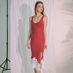 a woman standing in front of a white backdrop wearing a red dress with lace trims