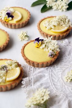 small lemon tarts with flowers and petals on a white table cloth next to lace