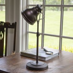 a desk lamp sitting on top of a wooden table next to a book and window