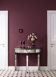 a table with vases and candles on it in front of a purple painted wall