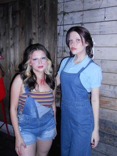 two young women dressed in overalls and makeup posing for the camera with one woman's face painted red