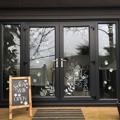 an open sign in front of a glass door with flowers on it and a chalkboard