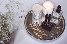 an assortment of beauty products on a tray next to a vase with flowers and candles