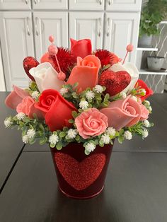 a vase filled with lots of red and pink flowers on top of a wooden table