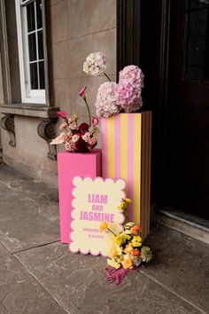 pink and yellow boxes with flowers in them sitting on the side of a building next to a door