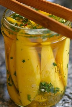 a jar filled with pickles sitting on top of a counter next to a wooden spoon