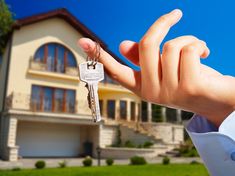 a hand holding a house key in front of a large home with the words dej written on it