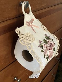 a white toilet paper roll hanging from a wooden drawer with lace and flowers on it