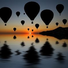 many hot air balloons are flying in the sky over water at sunset, with trees reflected in the water