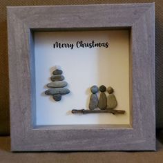 a frame with some rocks in it that says merry christmas and two people sitting on a tree branch