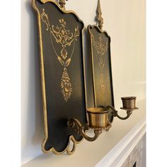 an ornately decorated wall mounted candle holder on a white mantel with two candles