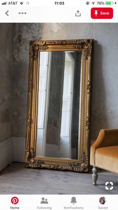 a large gold framed mirror sitting on top of a wooden floor next to a chair