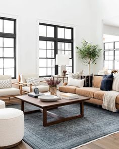 a living room with couches, chairs and tables in front of two large windows