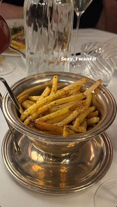 a silver bowl filled with french fries on top of a white tablecloth covered table