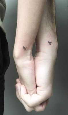 two people holding hands with small tattoos on their arms and one has a heart in the middle