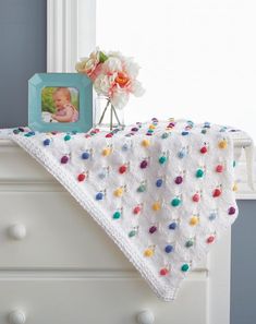 a crocheted baby blanket on top of a dresser next to a vase with flowers