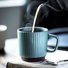 a coffee cup with steam pouring out of it sitting on top of a table next to a book