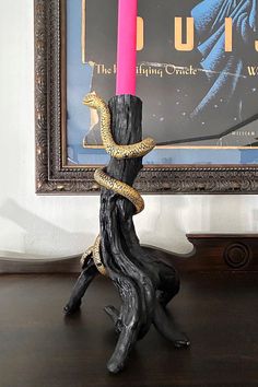 a candle with a snake wrapped around it sitting on a table next to a framed poster