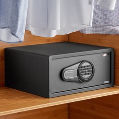 a black safe sitting on top of a wooden shelf next to a white shirt and blue towel