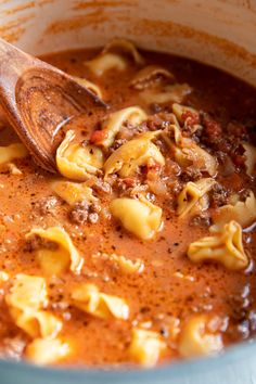 a wooden spoon in a pot filled with pasta and meat sauce on top of a table