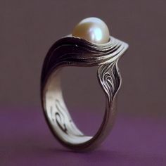 a close up of a ring with a pearl in the center on a purple surface