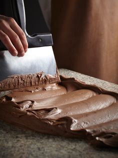 a person is spreading chocolate frosting on top of a cake with a large knife