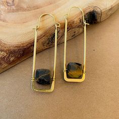 A uniquely fresh and new twist on a modern hoop style earring. We’ve suspended cube gemstones inside the negative space of a rectangle shaped wire hoop. The base of the hoop is hammered flat and tapers up the sides. These earrings are ultra lightweight and very comfortable to wear. ⬩7-9mm x 7-9 mm Cube shape Gemstone ⬩Hoop and Hook style brass wire ⬩2.5 inch Hoop earring ⬩Available in Amazonite, Labradorite, Moonstone, and Tiger Eye This item will ship with gemstone information on the Santore Je Art Jewelry Earrings, Hammered Jewelry, Jewelry Organizer Wall, Cube Necklace, Cube Shape, Brass Hoop Earrings, Bar Jewelry, Gem Shop, Rectangle Earrings