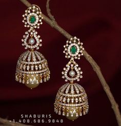 pair of earrings with pearls and emerald stones hanging from tree branch against red background, closeup