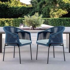 two blue chairs sitting next to each other on top of a cement floor near a table