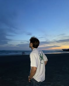 a young man standing on top of a beach next to the ocean at sunset or dawn