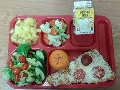 a red tray with pizza, salad and fruit on it sitting on top of a wooden table