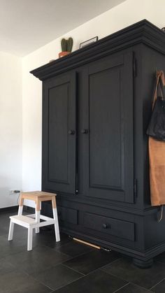 a black armoire sitting on top of a floor next to a wooden stool and bag