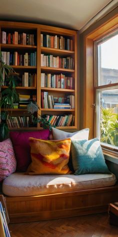 a couch with many pillows in front of a bookshelf filled with lots of books