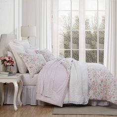 a bed with white sheets and pink flowers on it in front of a large window