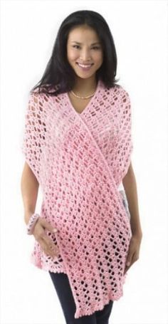 a woman standing wearing a pink crocheted ponchy with one hand on her hip