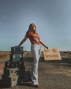 a woman holding a sign standing next to suitcases in the middle of an empty road