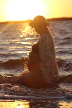 a pregnant woman sitting in the ocean at sunset