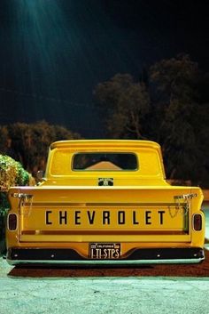 the back end of a yellow chevrolet truck parked in front of a house at night