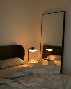 an unmade bed with two lamps on each side and a mirror in the corner