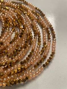 Elastic Waist Bead "Koun-Fao" crafted with resplendent gold glass crystal seed beads and adorned with delicate light brown glass seed bead accents. This elastic waist bead not only emanates opulence but also embodies a warm and earthy elegance, offering a comfortable and adjustable fit that transcends beauty and symbolism. 🌟 Gold Glass Crystal Seed Beads - Opulent Radiance: Koun-Fao is adorned with a luxurious array of gold glass crystal seed beads, creating an opulent radiance that symbolizes Gold Festival Jewelry With Metal Beads, Gold Polished Waist Beads For Party, Bohemian Waist Beads With Spacer Beads For Party, Bohemian Multi-strand Gold Beaded Bracelets, Bohemian Waist Beads For Parties With Spacer Beads, Adjustable Waist Beads For Parties, Gold Waist Beads For Party, Bohemian Beaded Waist Beads For Parties, Bohemian Gold Multi-strand Beaded Bracelets