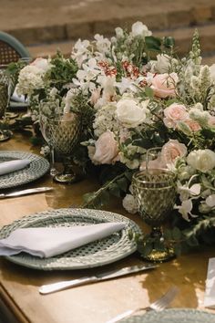 the table is set with plates, silverware and floral centerpieces on it