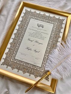 an ornate gold frame holds a certificate and feather quill on a white bed sheet