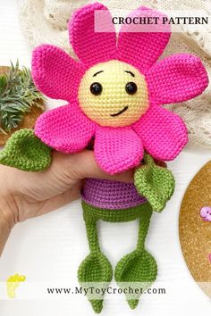 a crocheted pink flower with green leaves is held by someone's hand