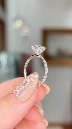 a woman's hand holding a diamond ring in front of her face, with white flowers on it